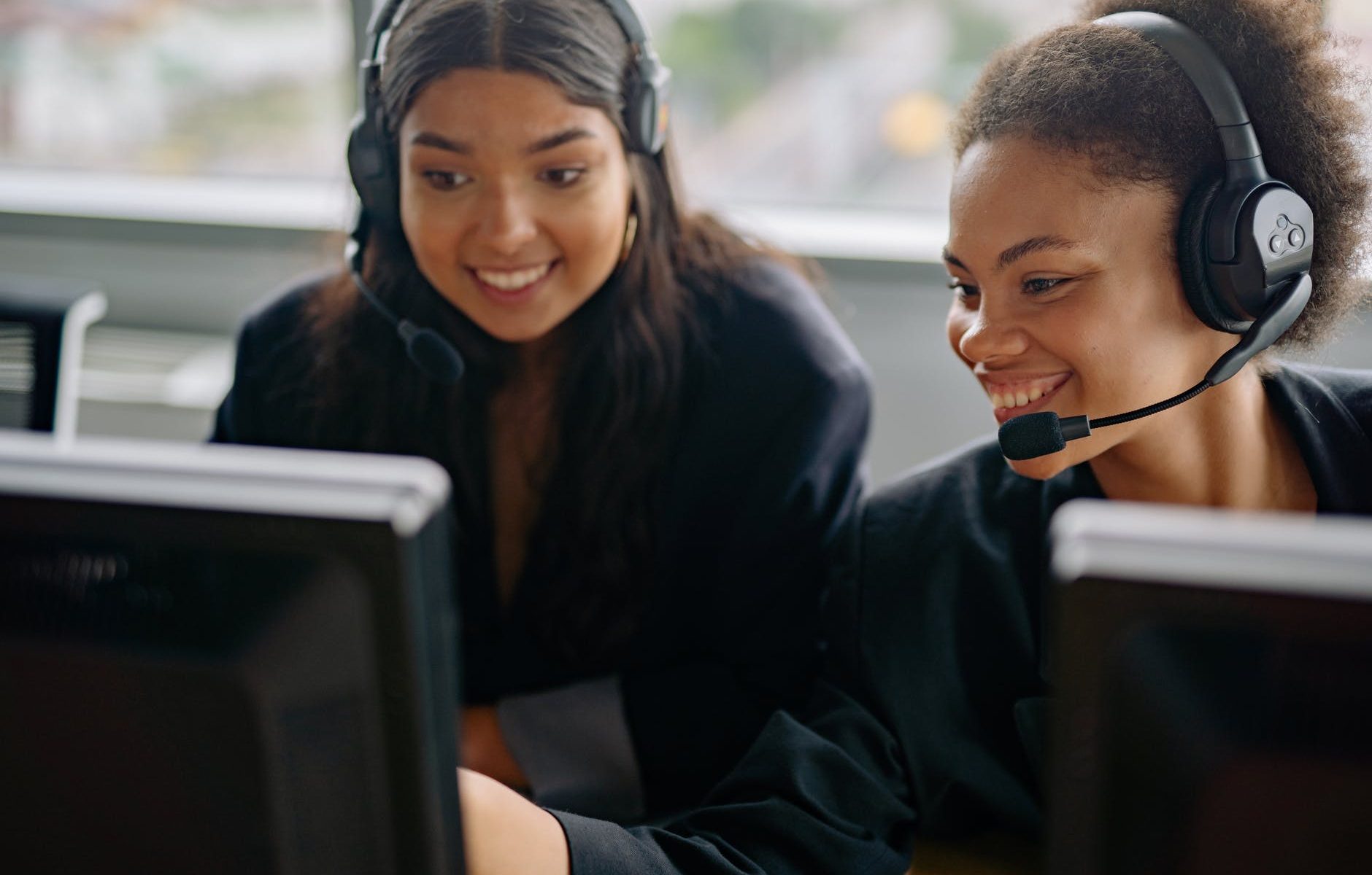 smiling women in black blazers wearing headsets looking at a computer monitor